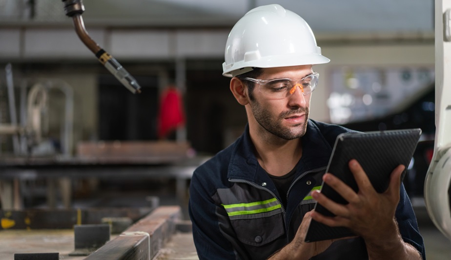 Worker with a hard hat checking production data on a tablet